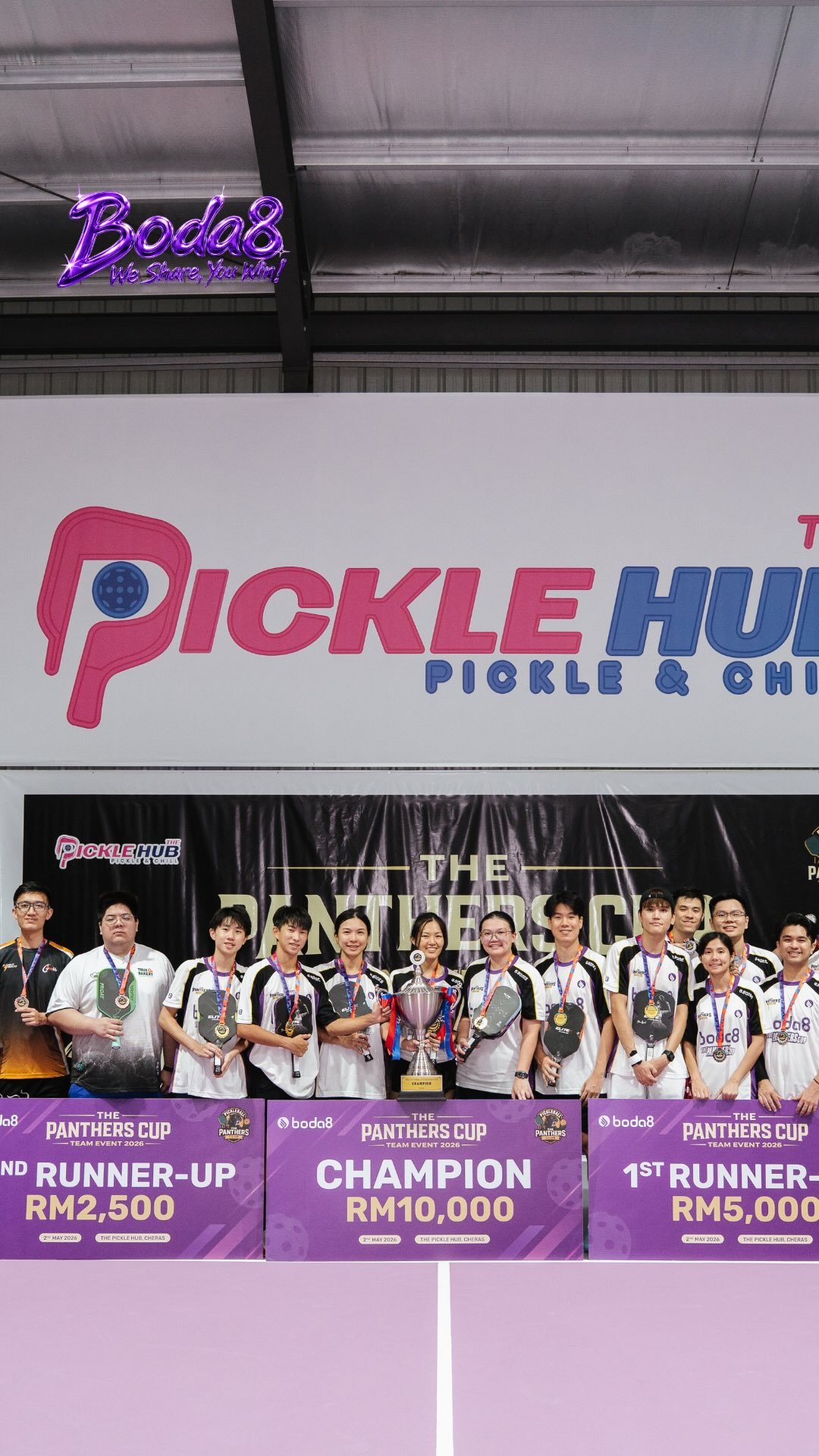 Boda8 Pickleball Team Event winners posing with medals, paddles, prize boards, and a trophy at The Pickle Hub.