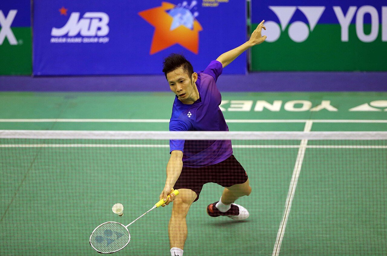 A badminton player reaches forward to play a shot at the net.