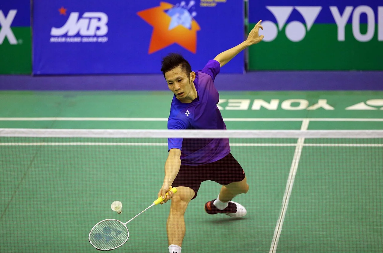 A badminton player reaches forward to play a shot at the net.