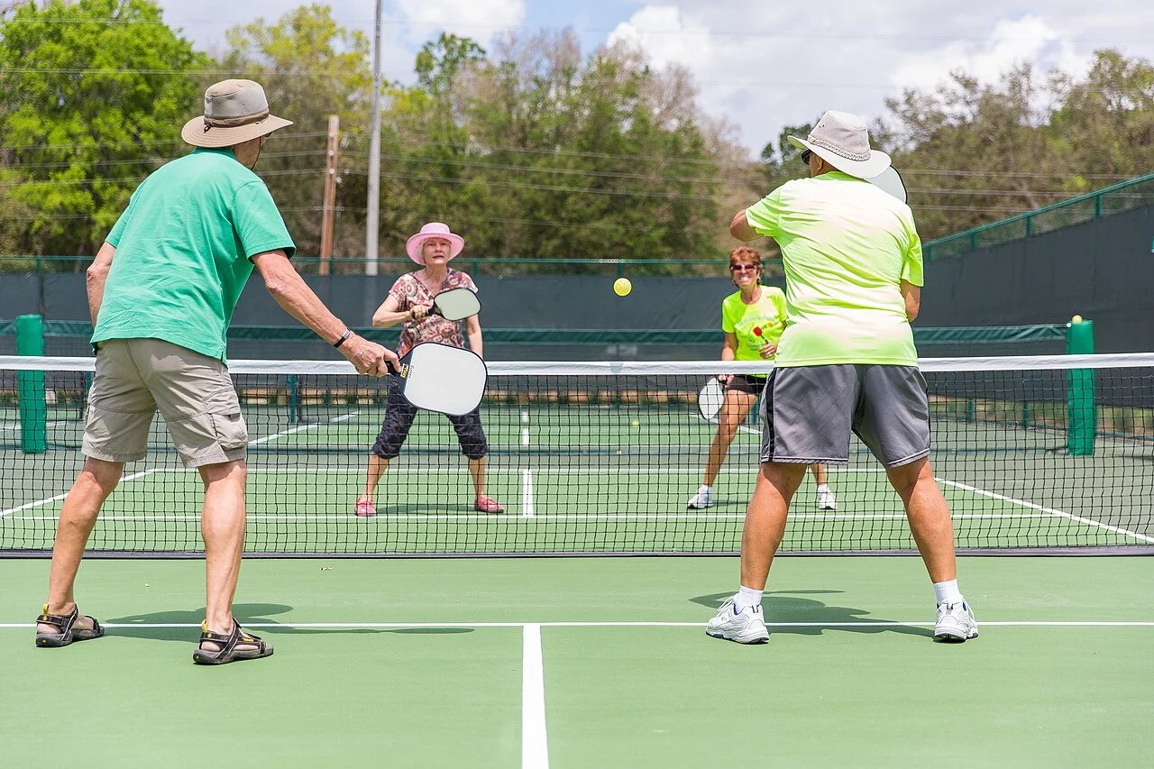 Four players exchange a shot during an outdoor pickleball game.