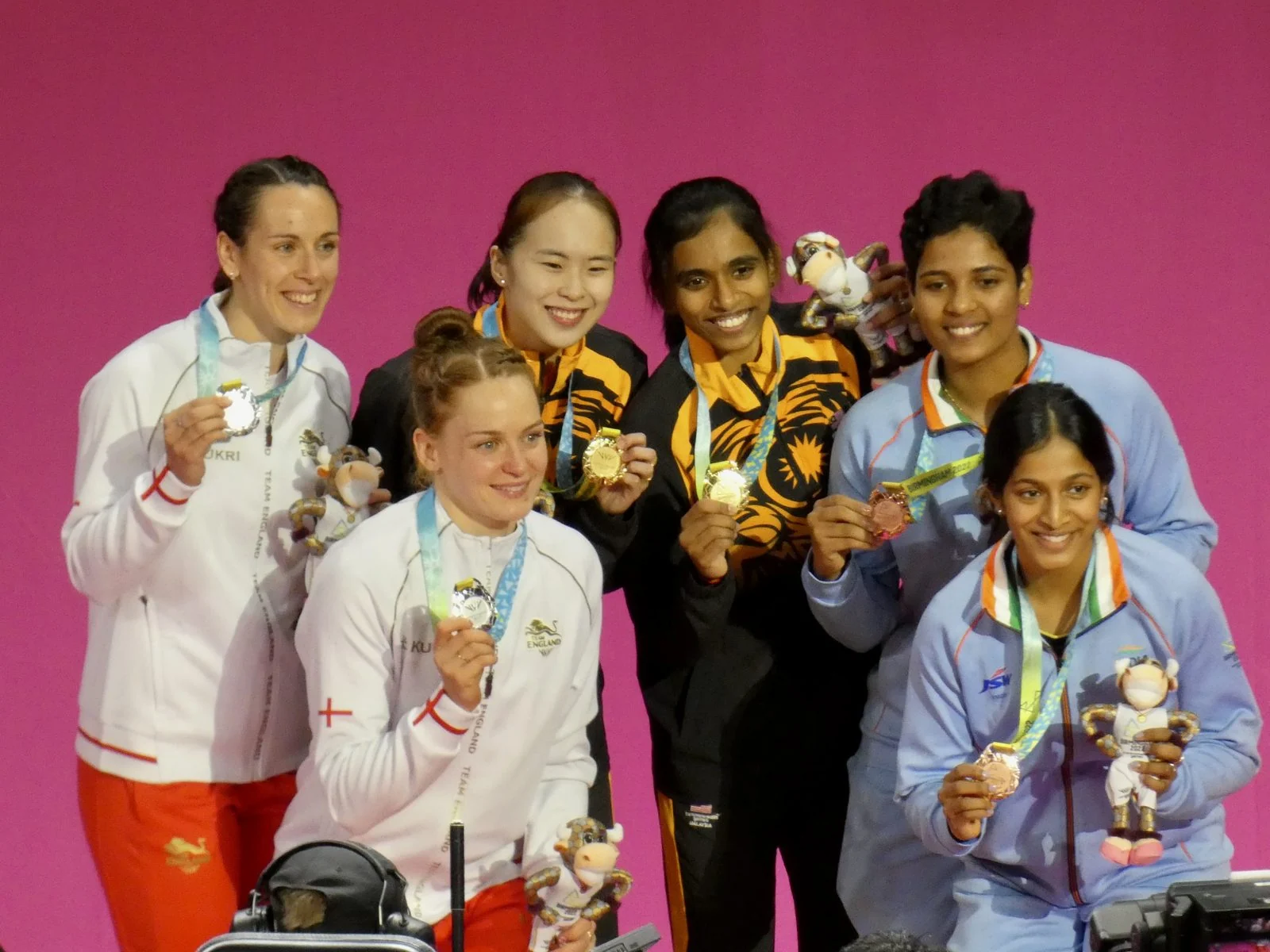 Three women's doubles badminton pairs stand on an international podium.