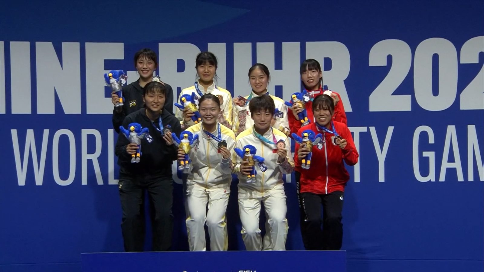 Women's doubles badminton medallists stand on a university games podium.